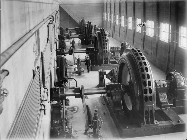 Elevated view of a man standing near the governors and generators inside the Prairie du Sac power house in 1915.